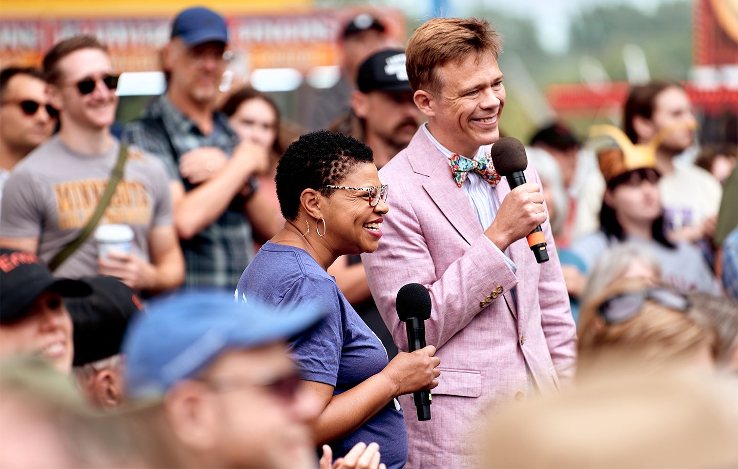 two adults standing with microphones in hand and surrounded by a crowd at the Minnesota State Fair